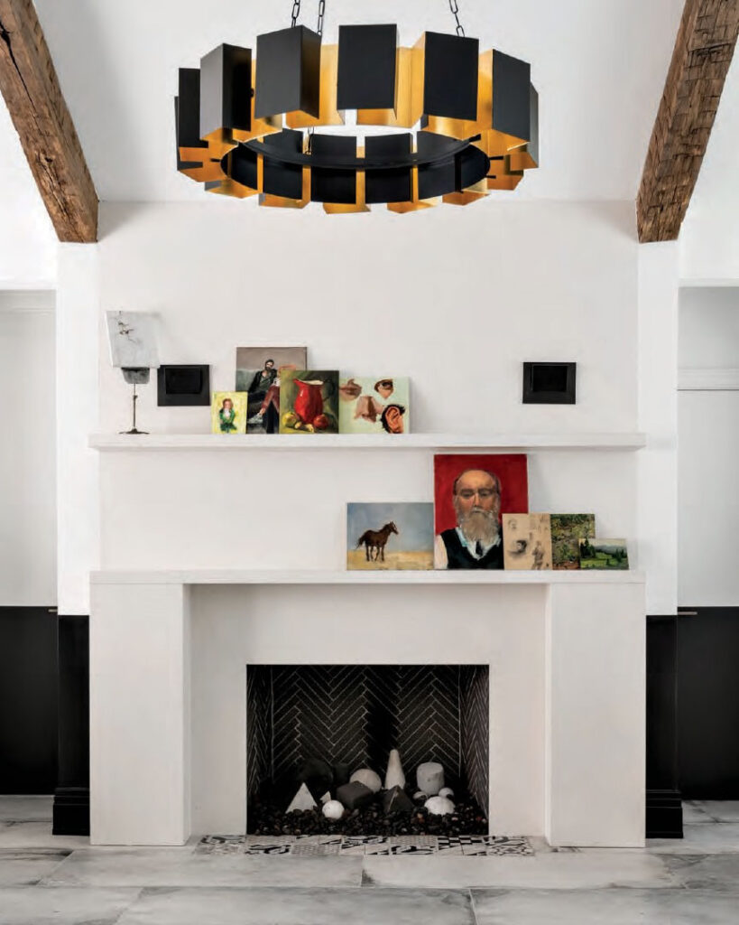 Luxe Interiors + Design Houston - Starting Fresh - A limestone fireplace with a custom two-tiered mantel warms the art studio. Framed by a pair of reclaimed wood beams, the Arteriors Vaughn chandelier adds drama with its substantial scale and glowing bronze finish