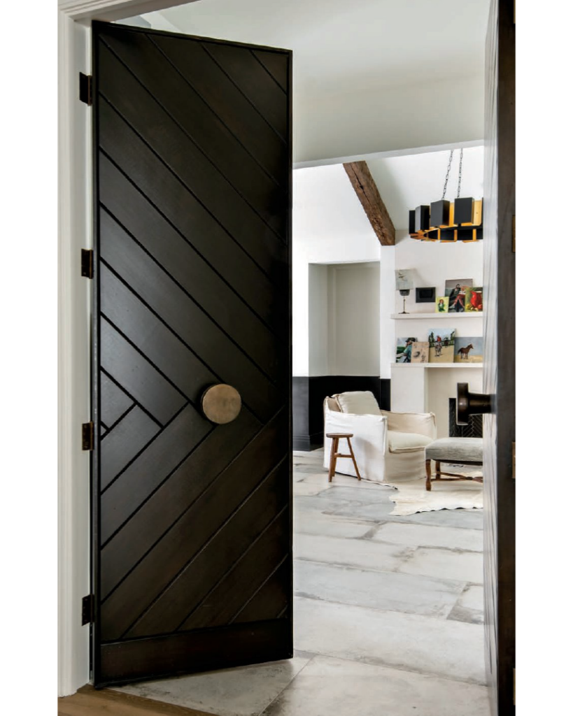 Luxe Interiors + Design Houston - Starting Fresh - Doors with a wood herringbone pattern designed by Chandos Interiors featuring brass knobs from Hollywood Builders Hardware open to a spacious second-floor art studio. Porcelain floor tiles from Pomogranit-ADR resemble timeworn stone pavers.